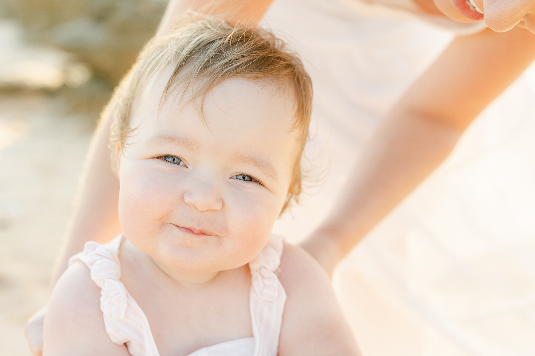 smiling baby girl in pink white striped dress on the beach with sunlight