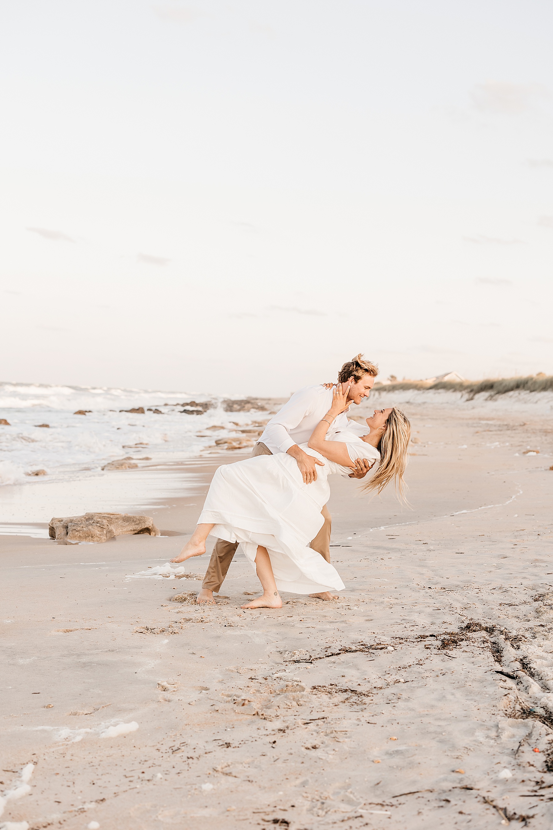 woman in white dress leaning back man holding her on the beach