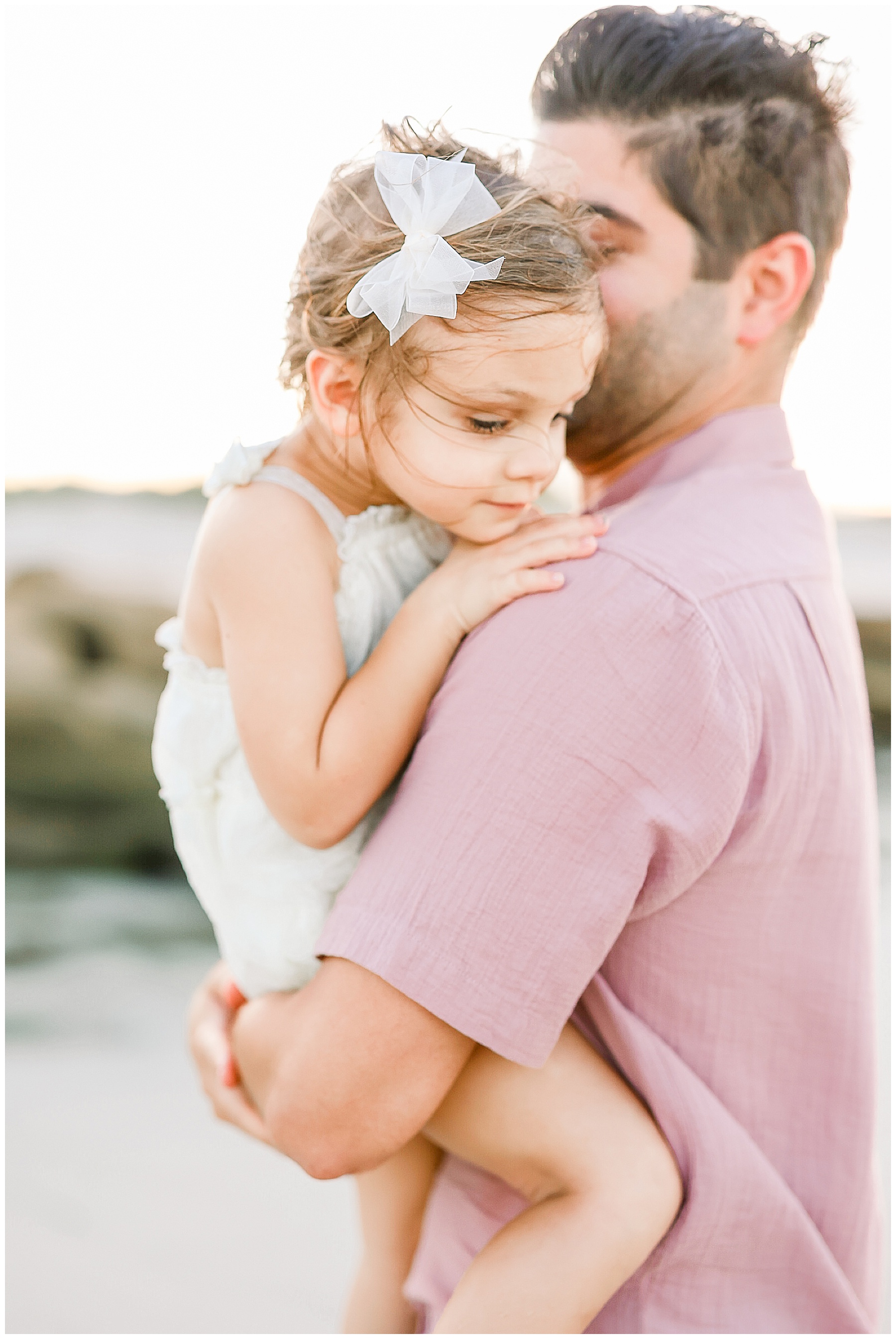 man holding little girl on the beach at sunset wearing pink shirt 