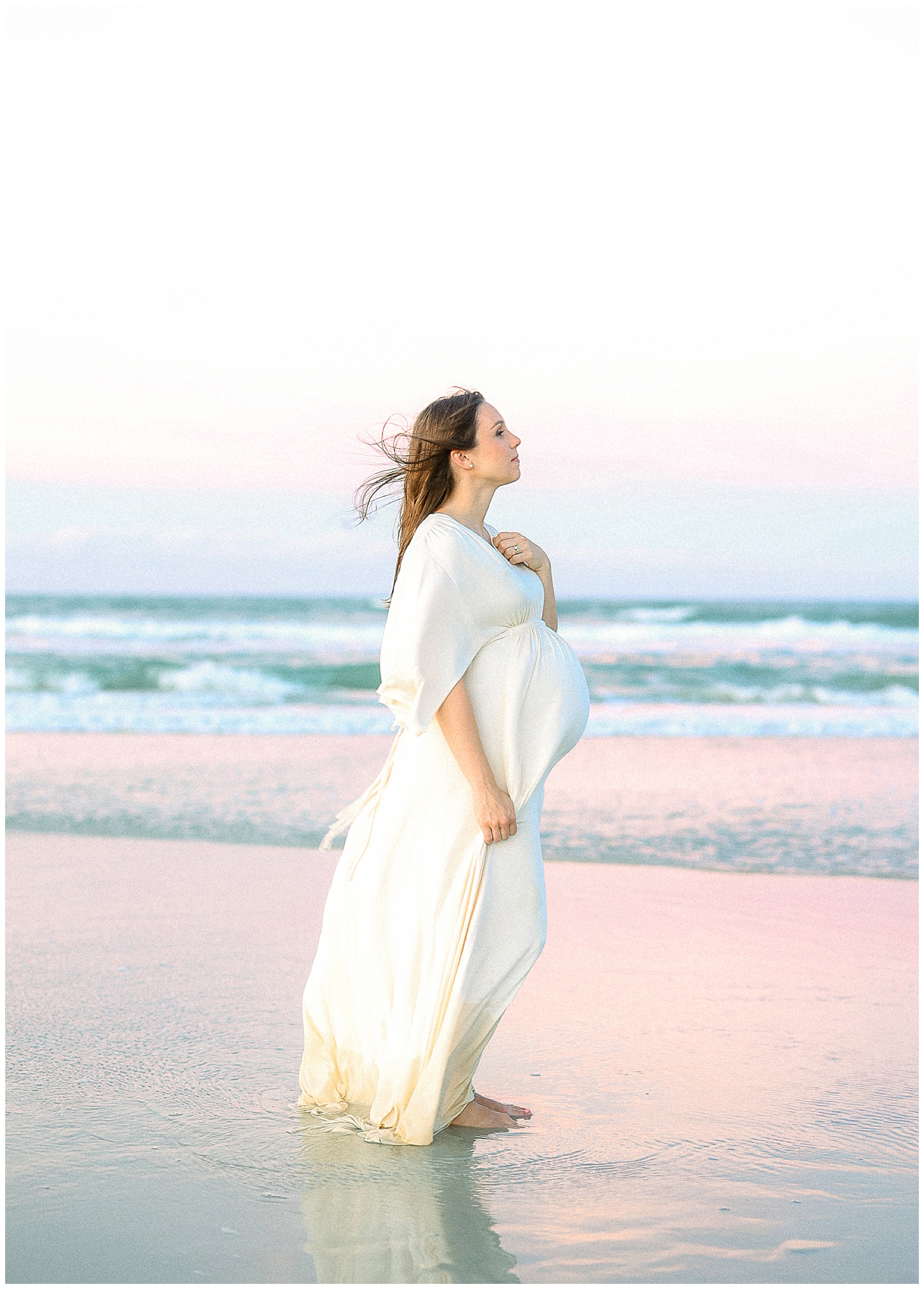 pregnant woman in cream maxi dress standing on the beach during a pastel sunset