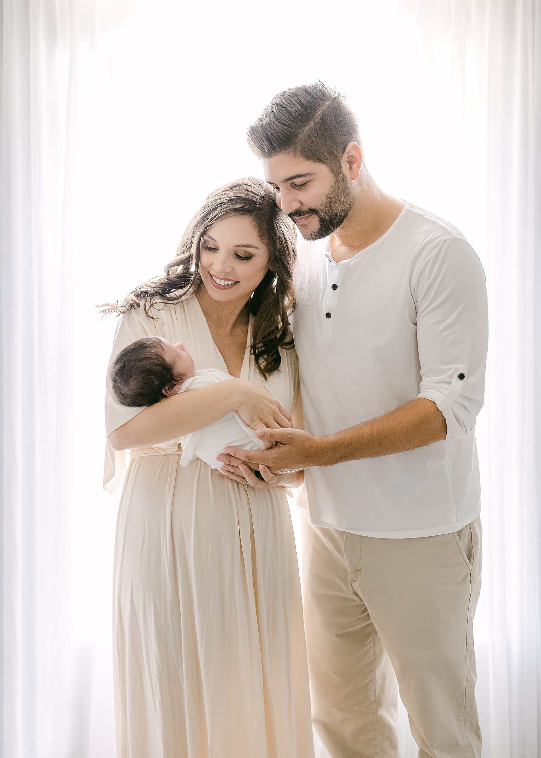 couple holding newborn baby boy in front of backlit light and airy window