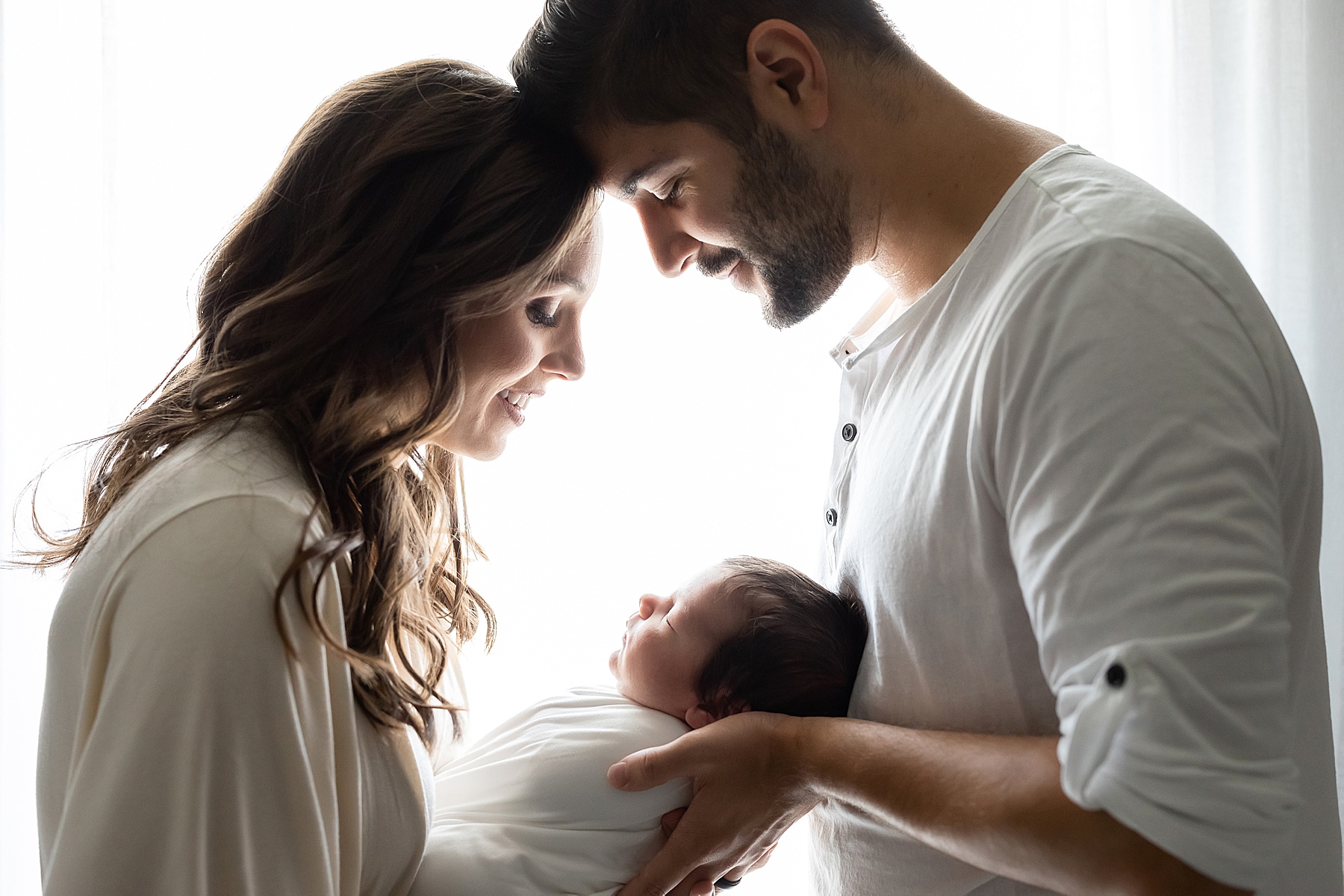 minimal image of couple holding newborn baby in front of light filled window
