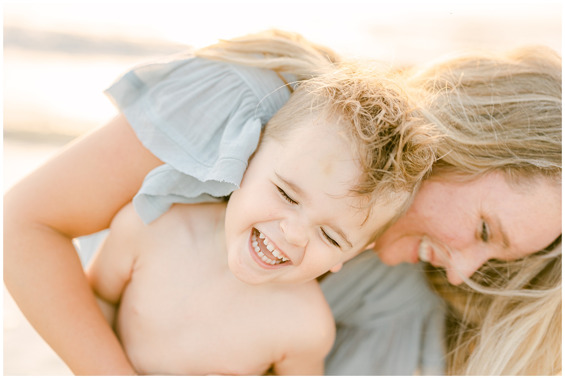 little boy laughiing with sage green colors at sunrise on the beach with mom