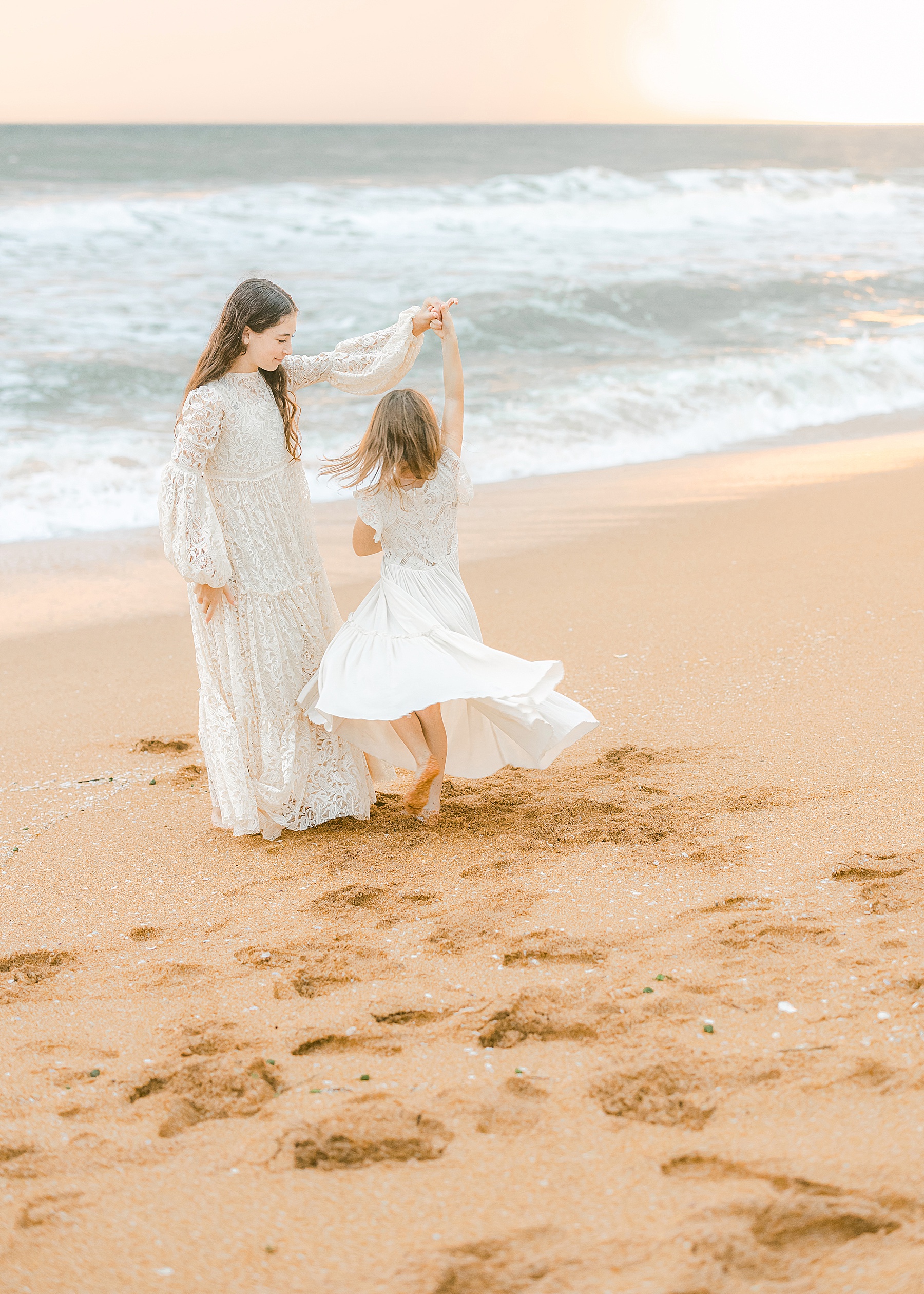 two girls wearing long white dresses dancing on flagler beach at sunrise