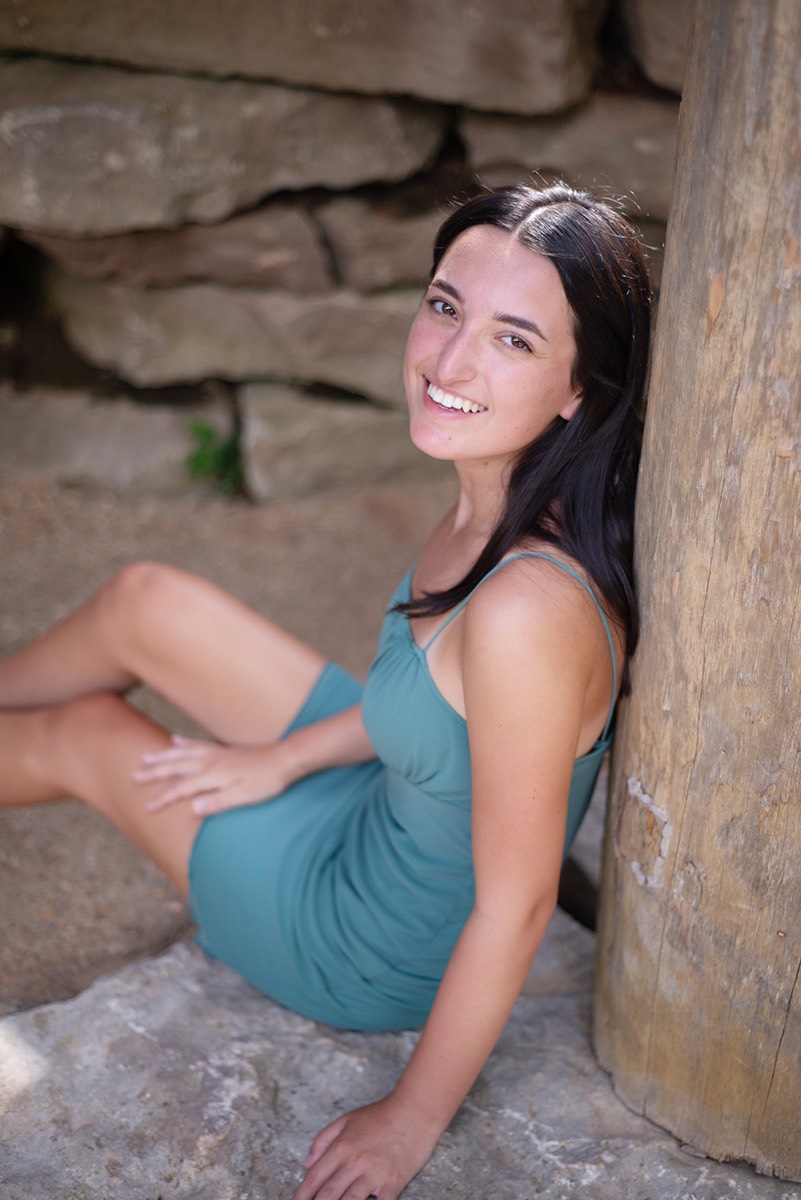 Senior girl in green dress sitting against wooden pillar at Dogwood Canyon.