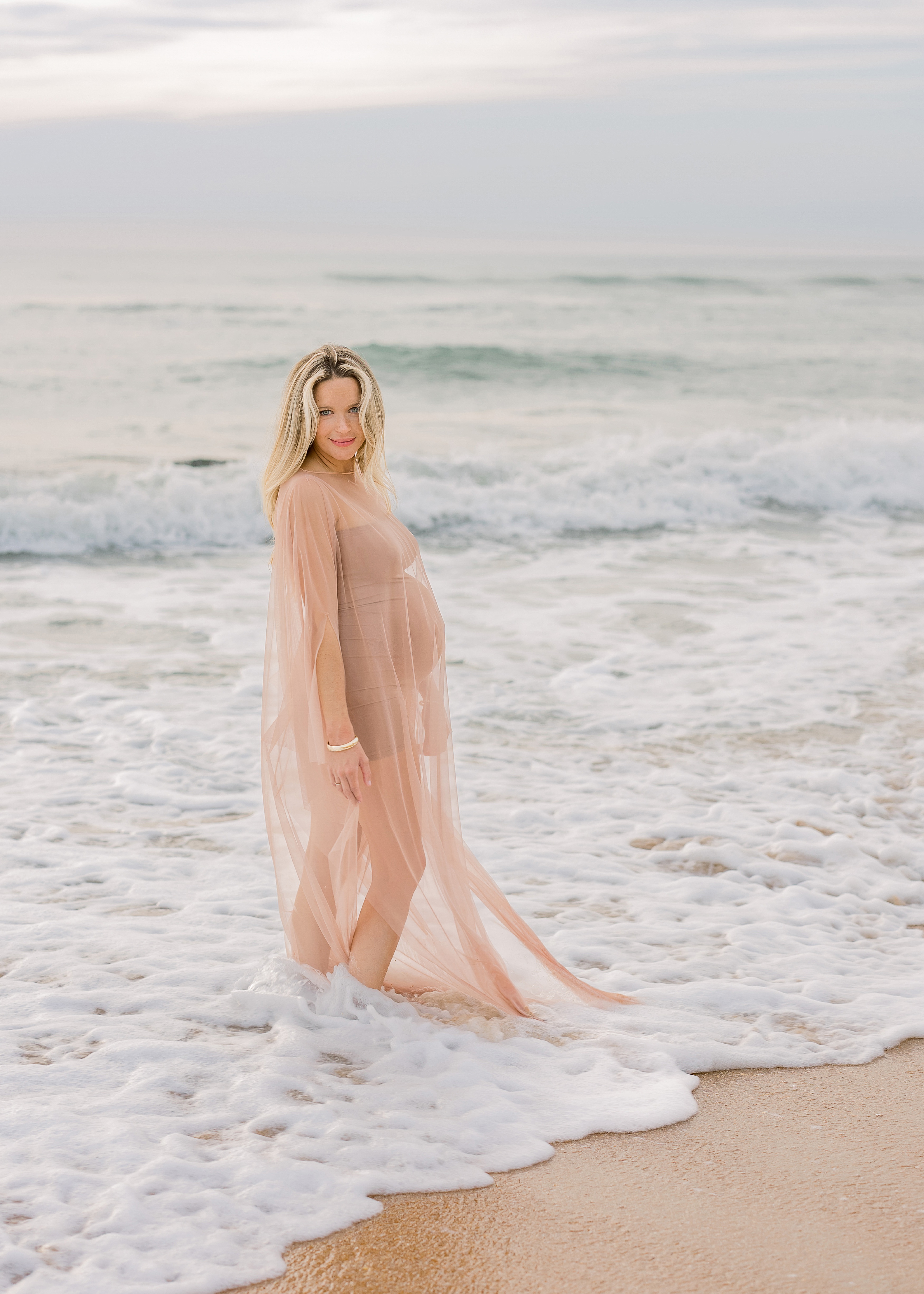 blond pregnant woman in nude tulle kimono at the beach at sunrise