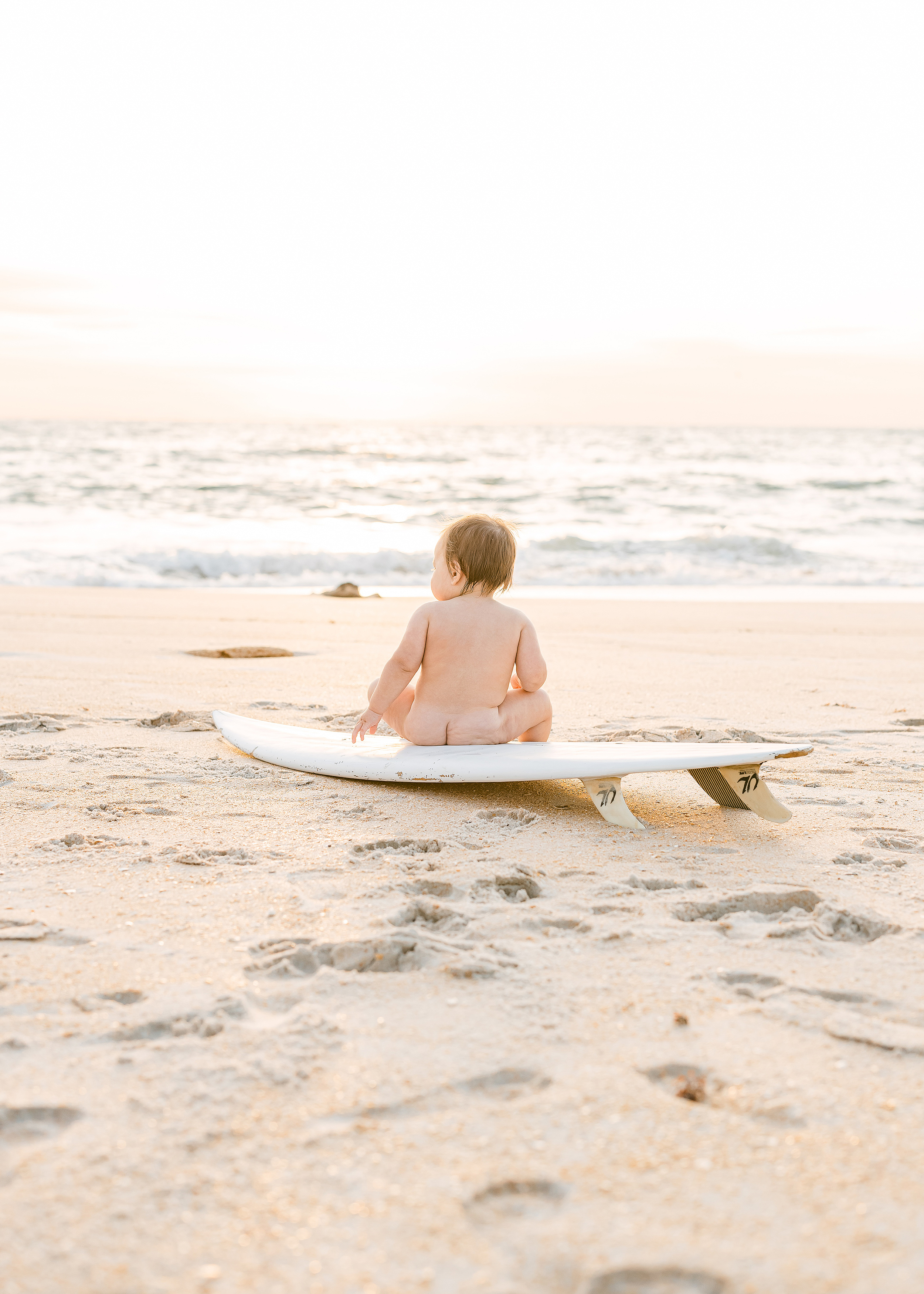 naked baby boy sitting on a surfboard at sunrise in Saint Augustine Beach Florida
