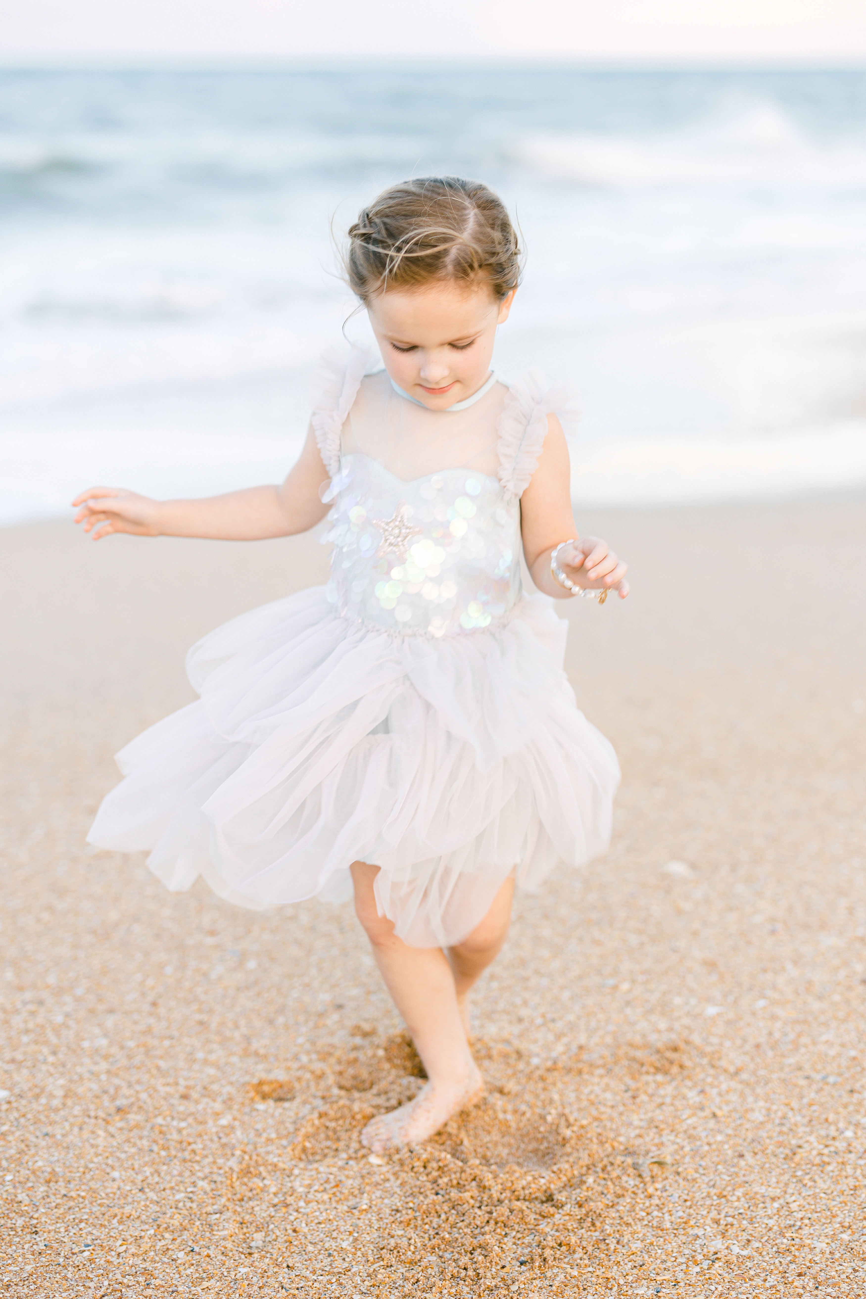 little girl dancing in a lavender tulle mermaid dress at the beach at sunset