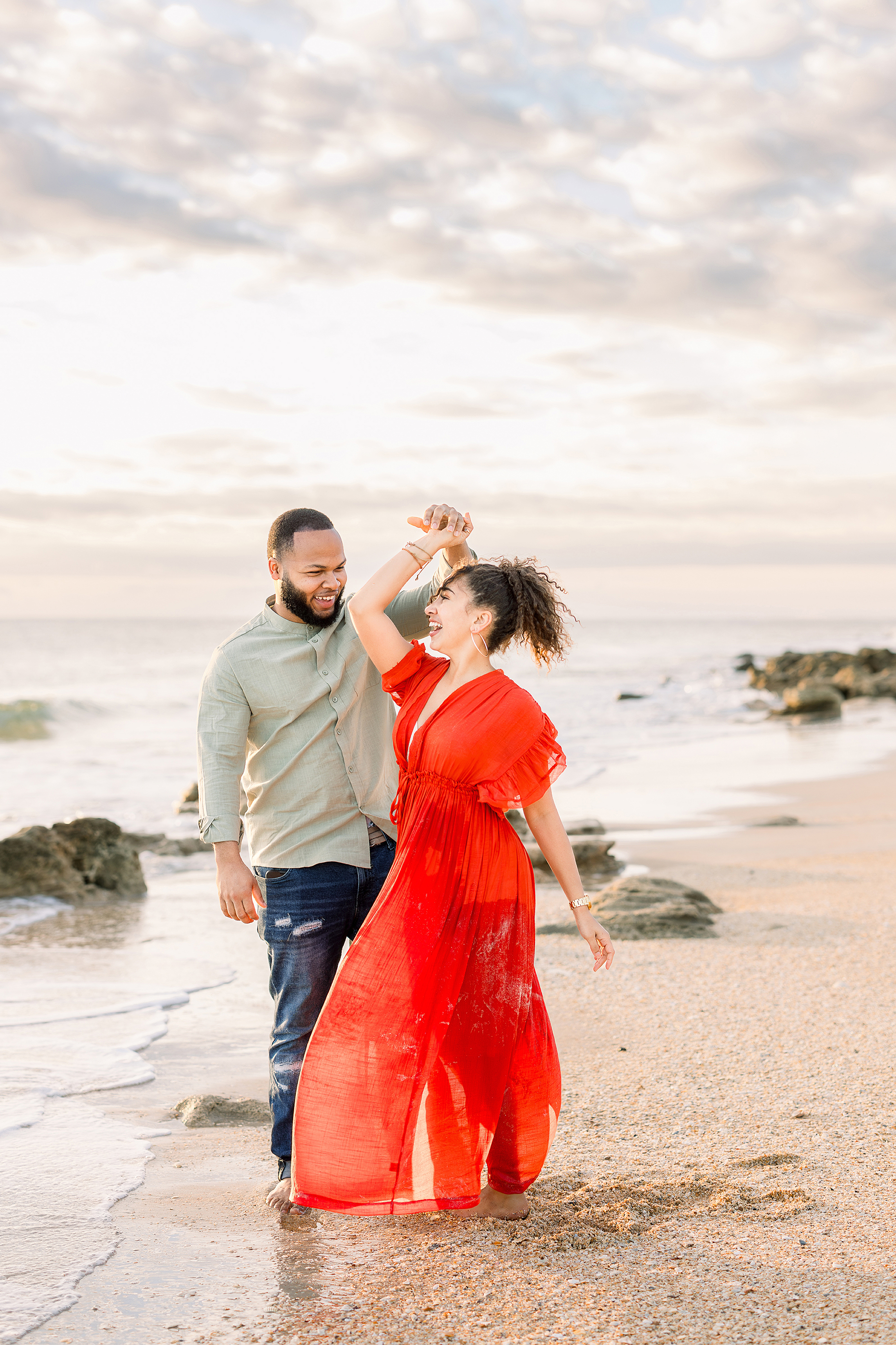 Woman in bright red dress dancing on the beach with a man at sunrise