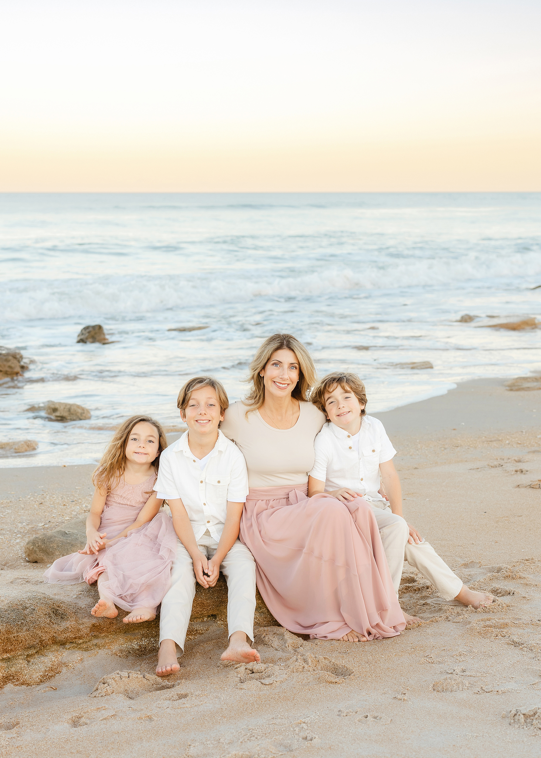 A mother with her children sitting on the rocks on the beach at sunset.