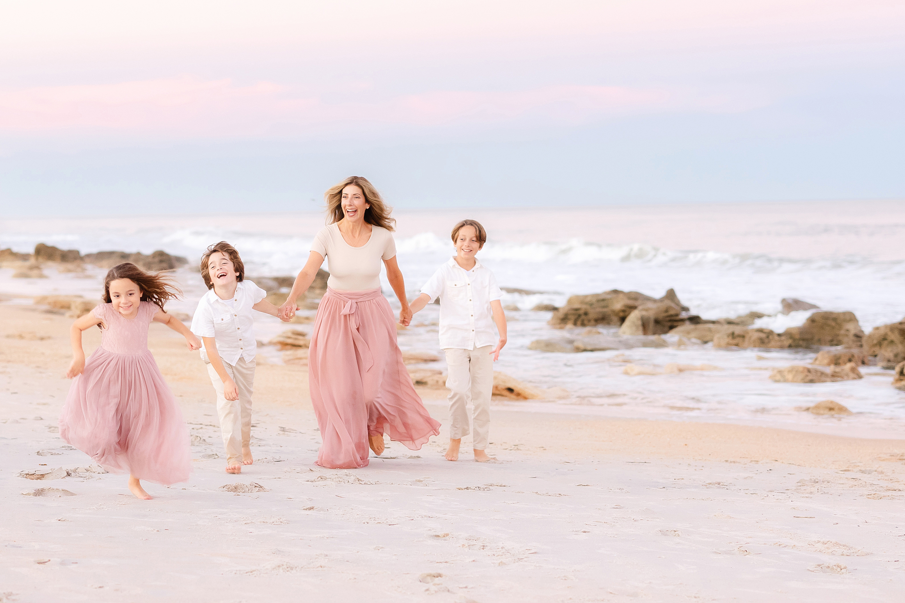 A pastel sunset beach portrait of children running with their mother on St. Augustine Beach.
