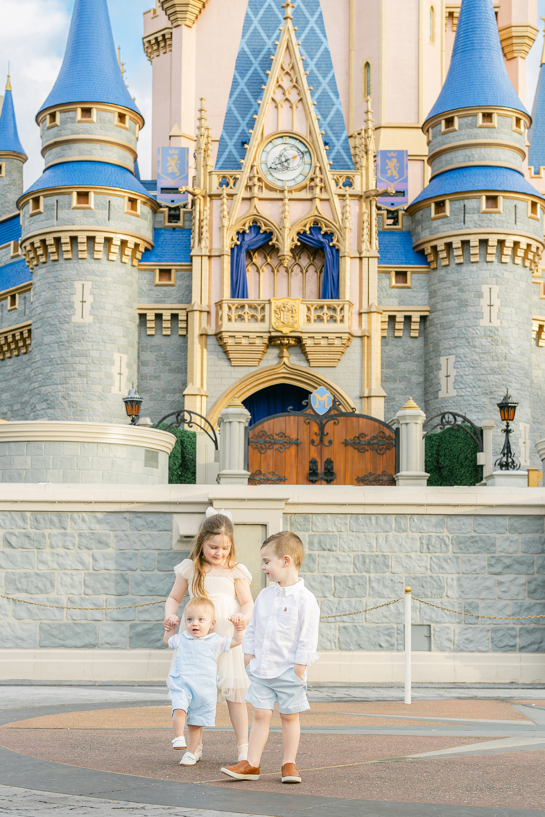 Three little children stand together in front of Cinderella's Castle.