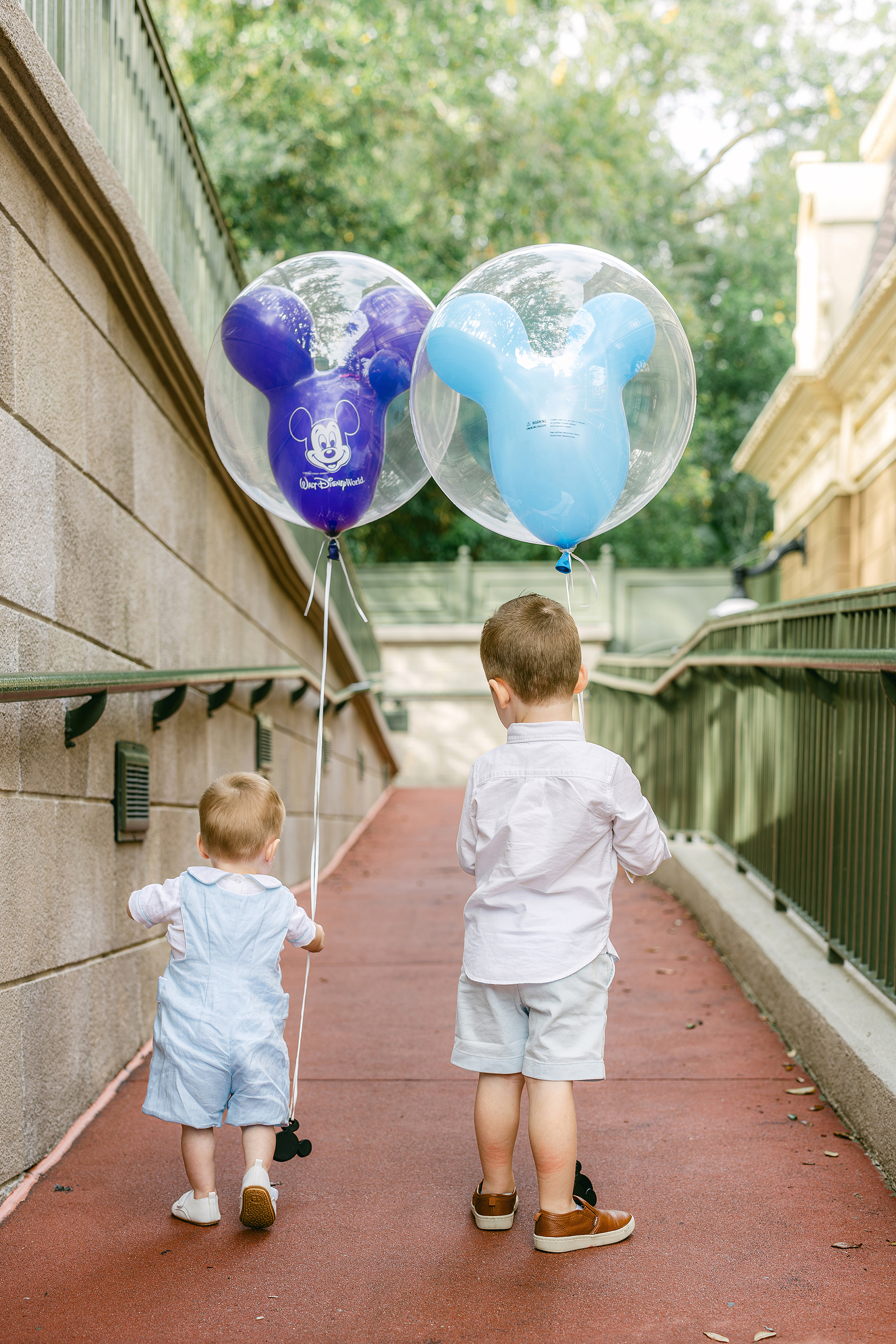 Two little boys walk together down a walkway holding Mickey Balloons.