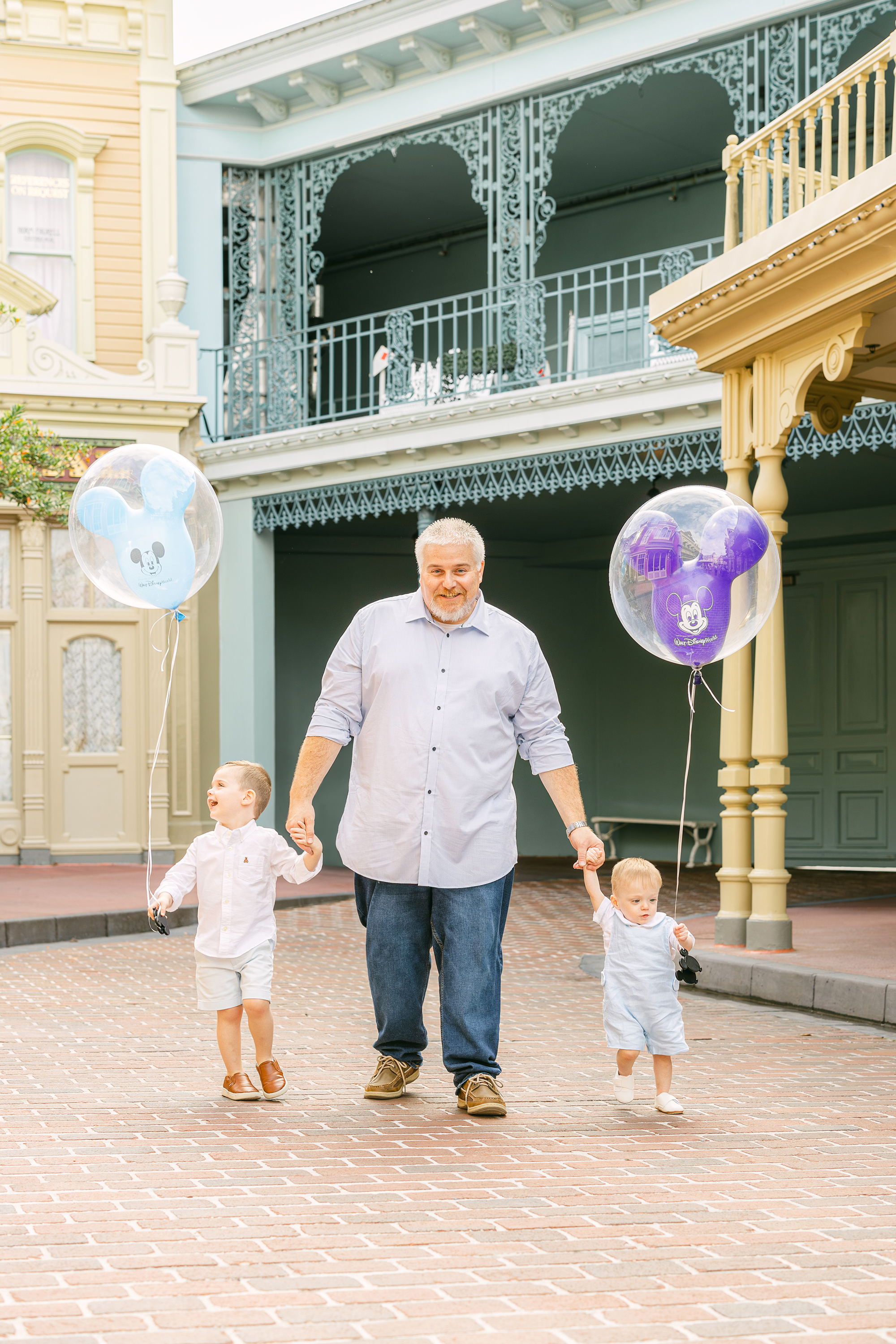 A father walks with his two sons who are holding Mickey balloons along Main Street U.S.A Disney World.