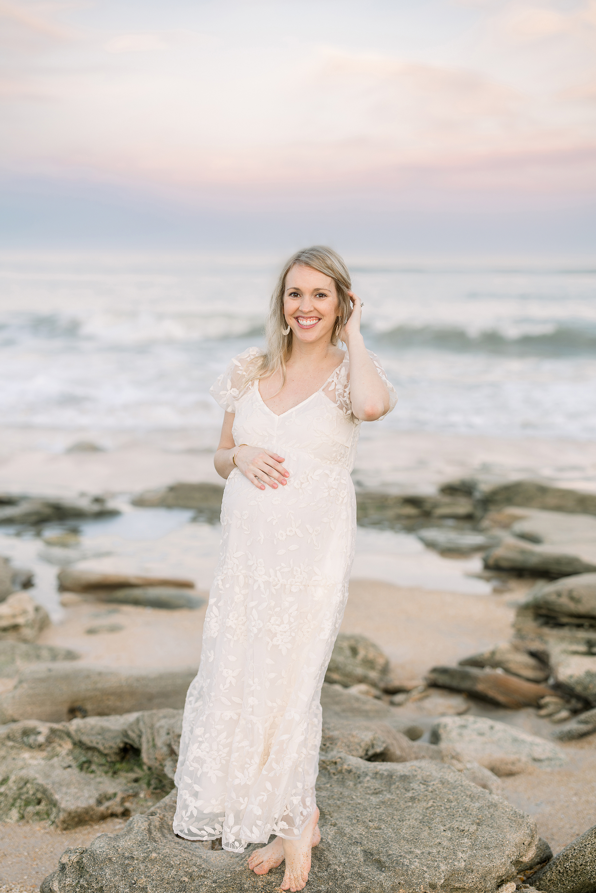 A sunset beach pregnancy portrait of a woman in a cream maxi dress.