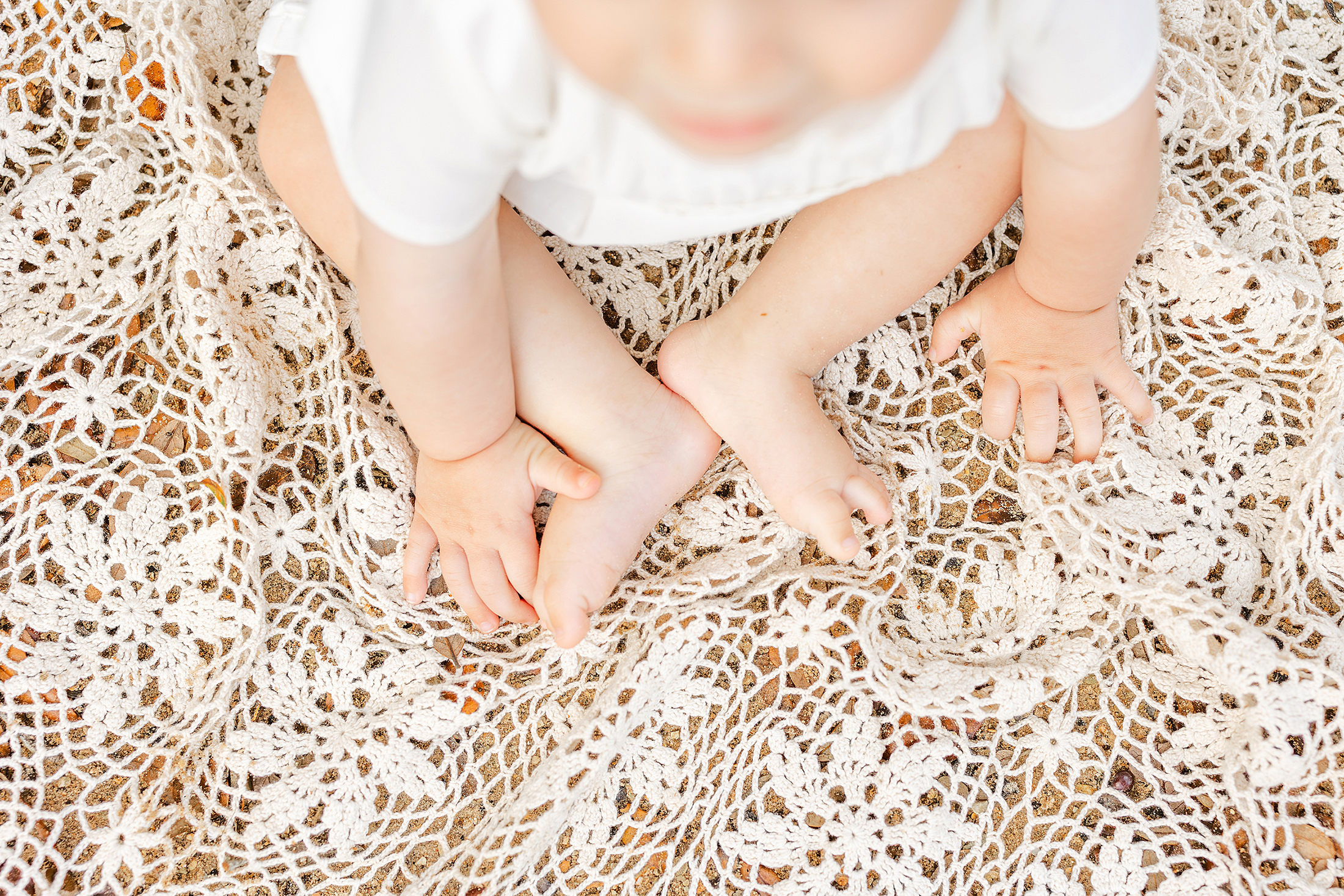 A light and airy portrait of a baby boy's feet sitting on a cream crochet blanket.