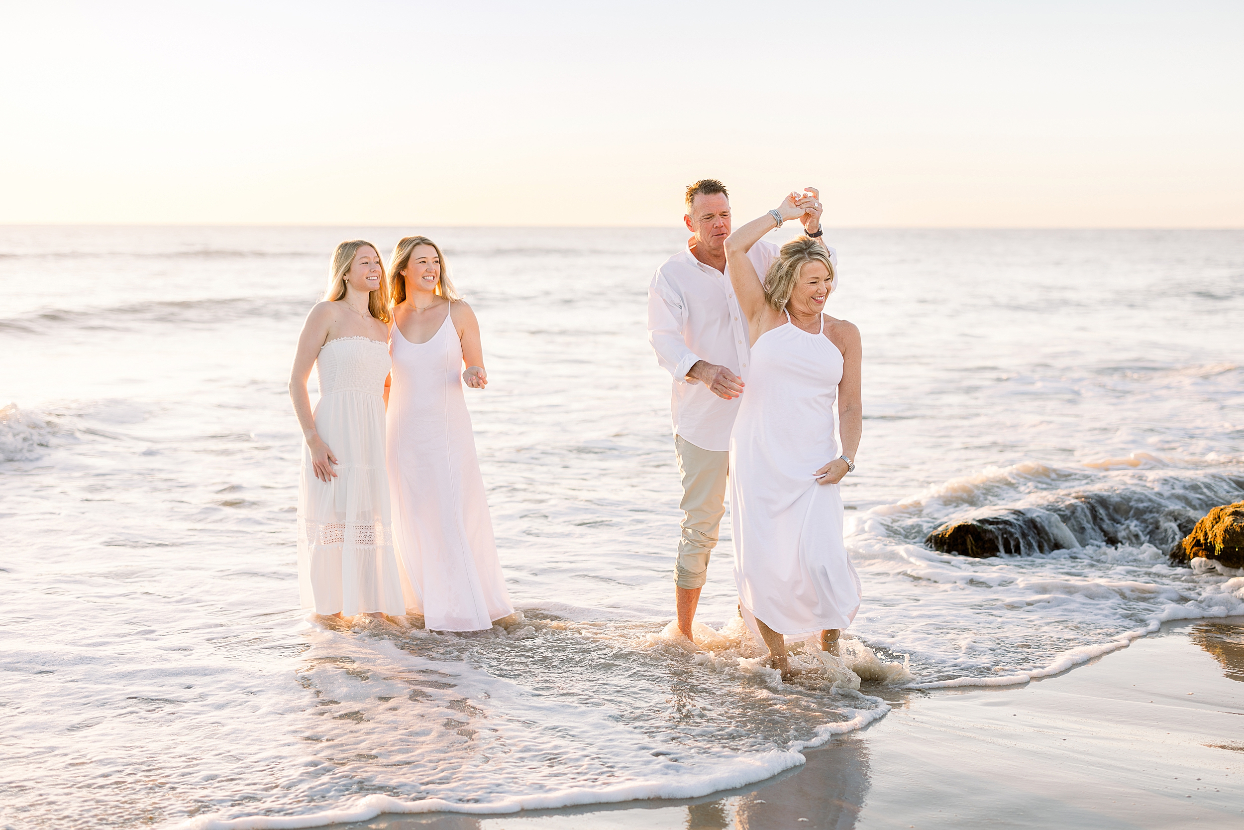 A family dressed in white playing together on the beach at sunrise.
