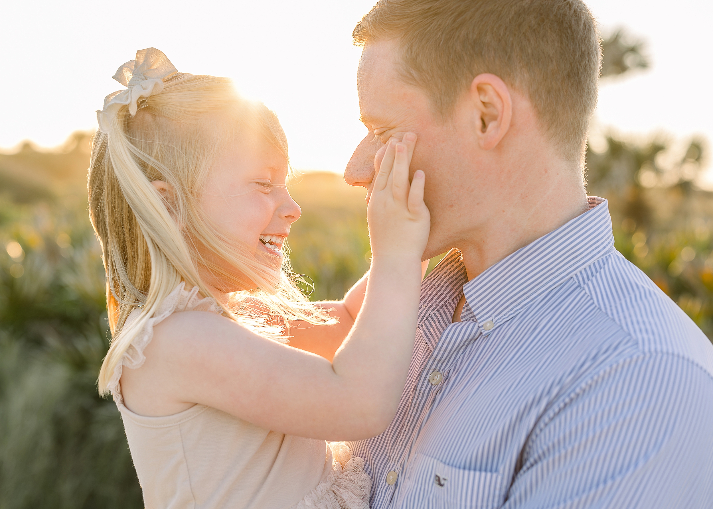 A light and airy sunset portrait of a father and daughter laughing and kissing.