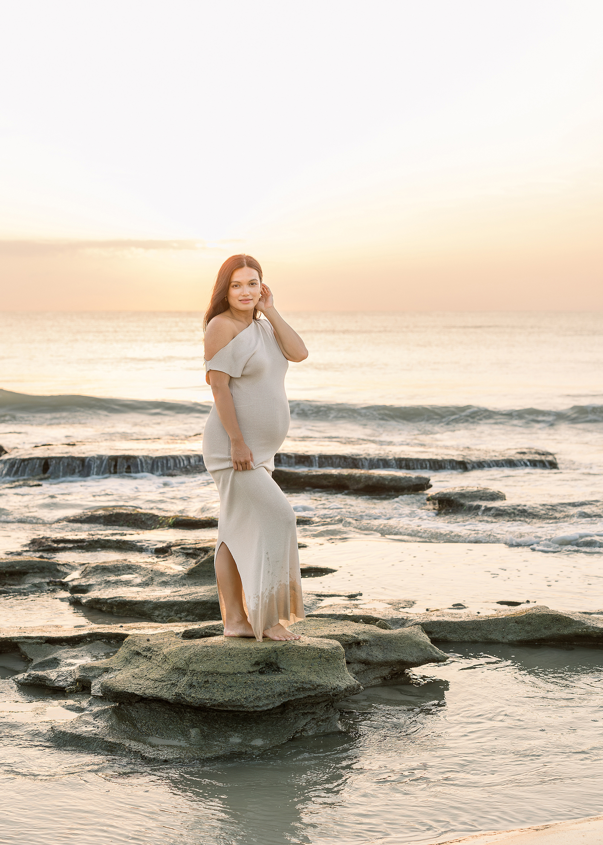 A sunrise maternity portrait of a woman standing on the rocks in Saint Augustine Beach, Florida.