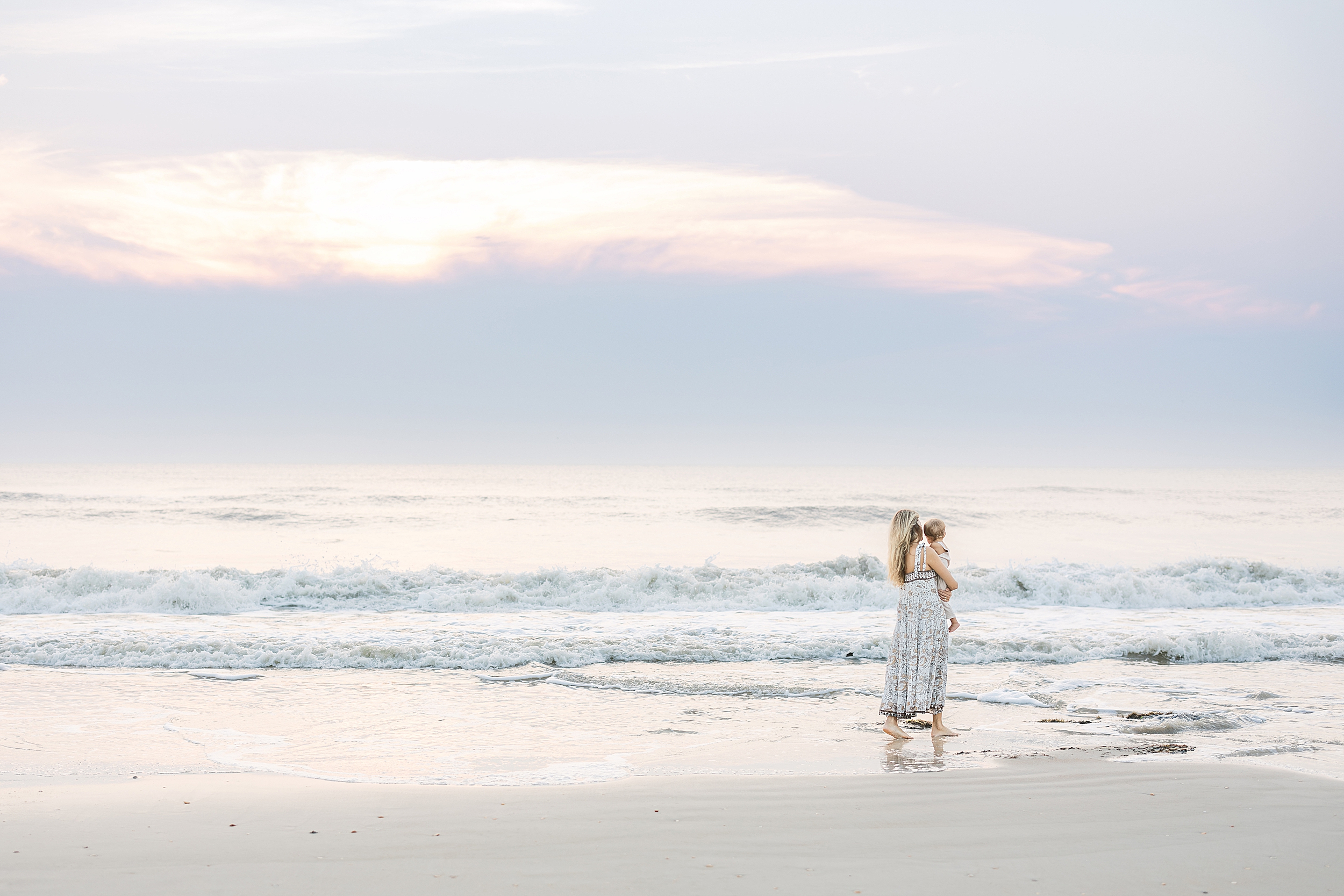 A pastel sunrise beach portrait of a woman holding her baby boy on St. Augustine Beach.