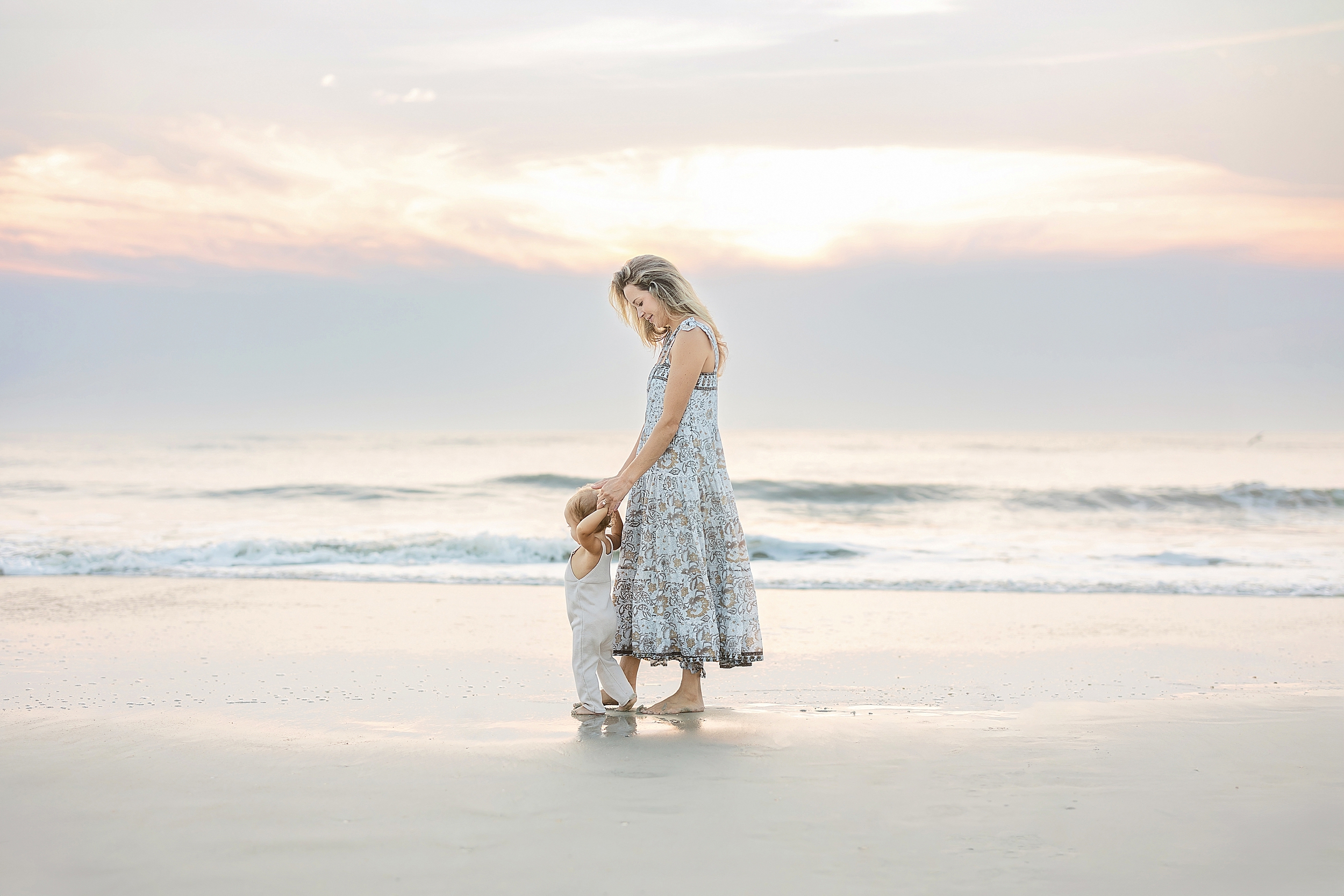 An ethereal sunrise motherhood portrait of a mother and her one-year-old baby boy at sunrise on the beach.