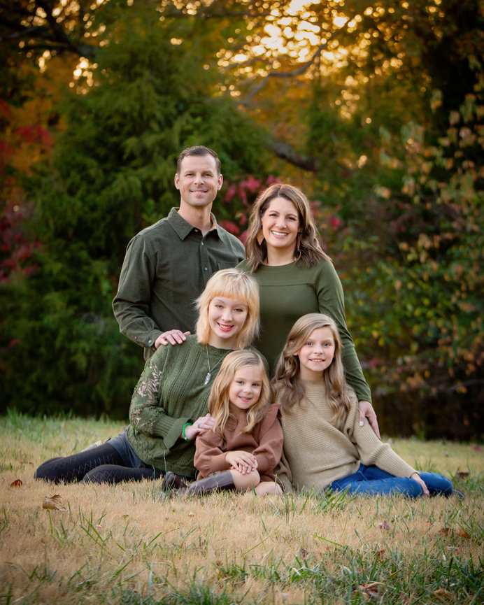 Family posing together in a grassy area with trees in the background during sunset.