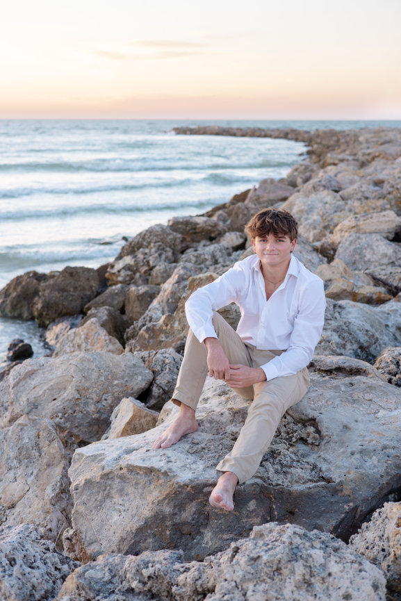 High school senior boy sitting on rocks at Sand Key Beach