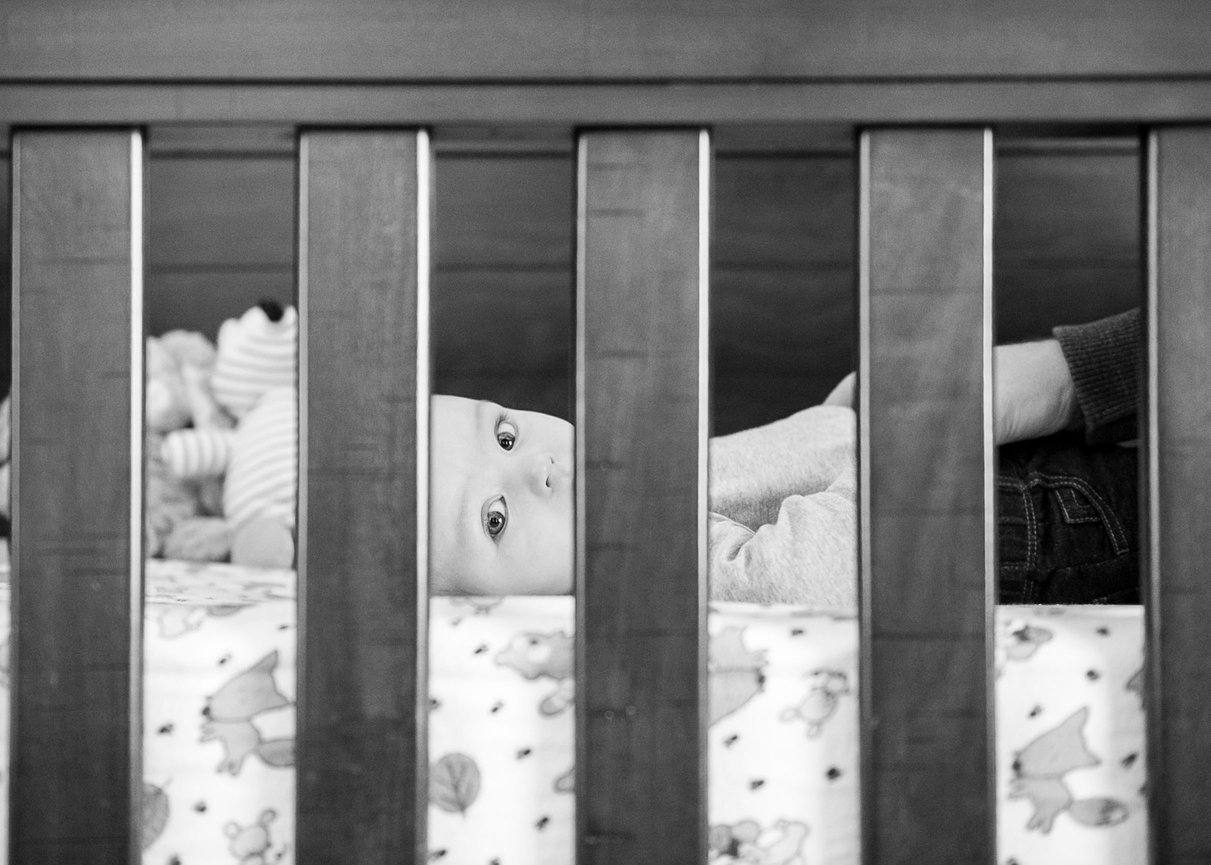 Baby glancing out through the slats in the baby bed.