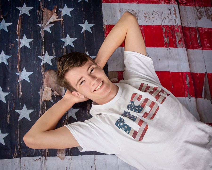 Smiling person lying on an American flag background wearing a white USA shirt.