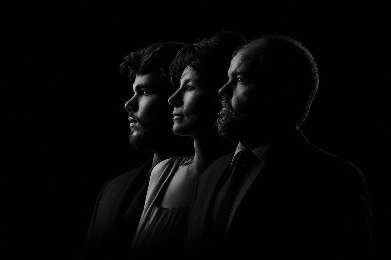 Three people in profile, side by side, in dramatic black-and-white lighting.