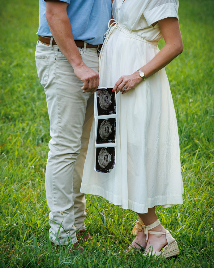 Pregnant couple holding ultrasound photos in a grassy field