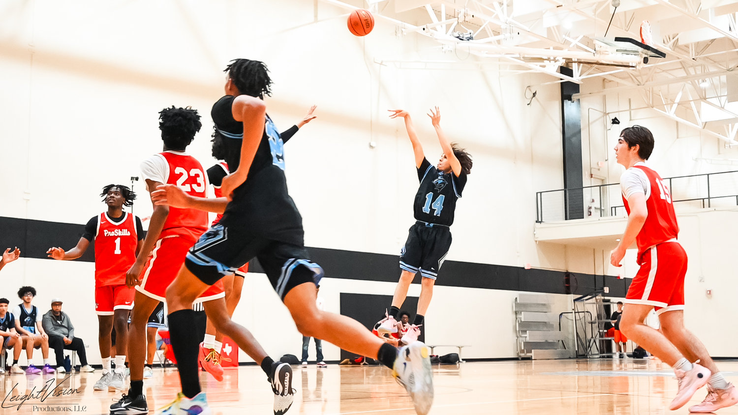 Boy in black jersey shooting a basketball while teammates and opponents are in action during a game.