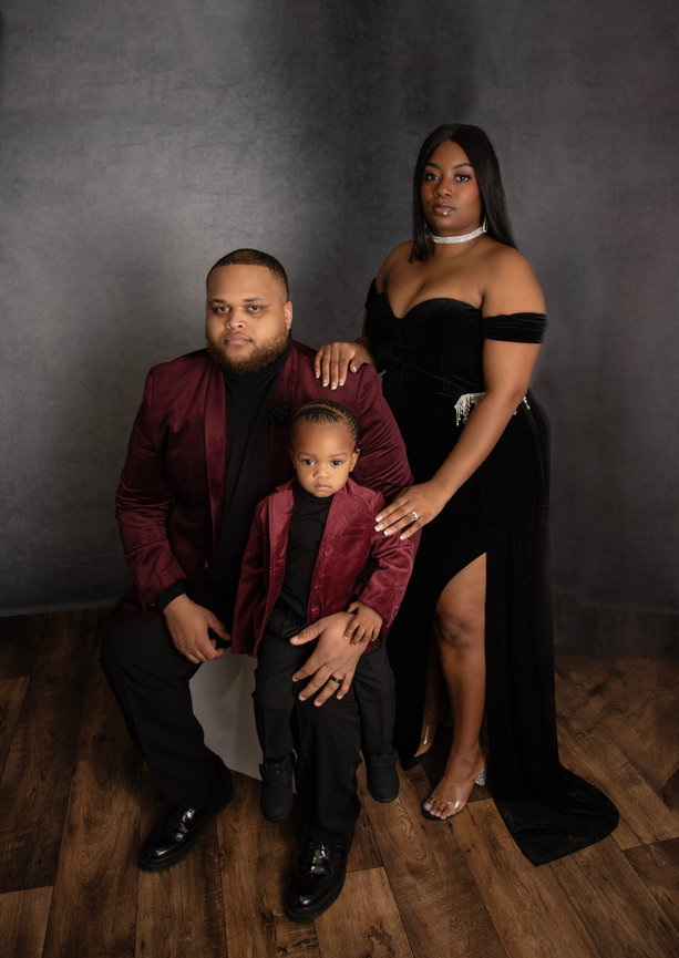Family portrait of a man and woman dressed in formal attire, seated with a young boy in a stylish outfit.