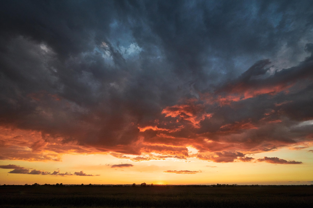 Dramatic sunset over a flat landscape with dark storm clouds and glowing orange sky