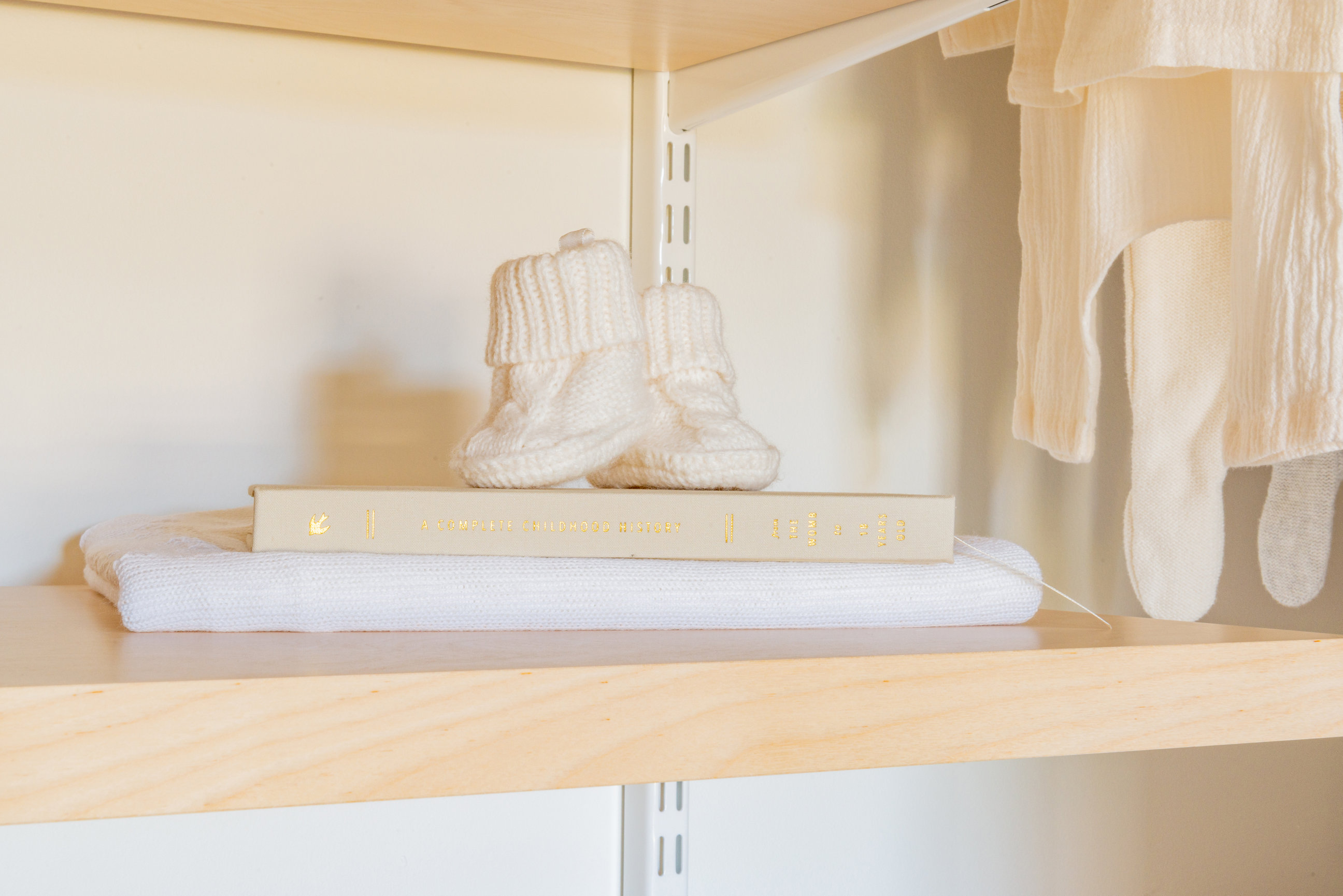 natural wood floating shelves in a nursery closet, cream colored sweater baby booties