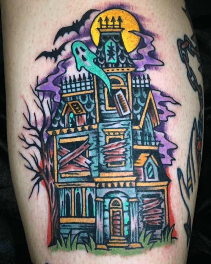 Colorful tattoo of a boarded up haunted house with bats and a ghost in the sky.