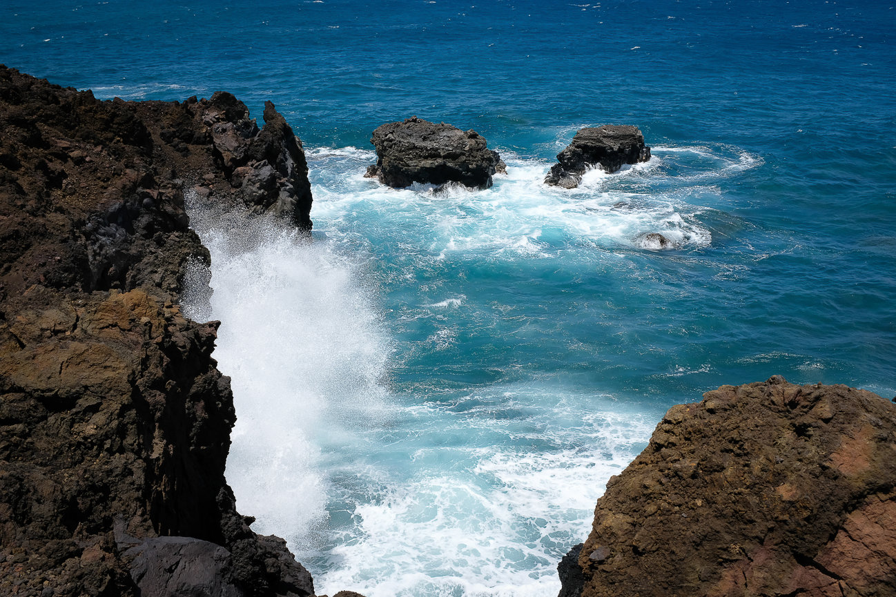 Ocean splashes into the lava shoreline in Maui.