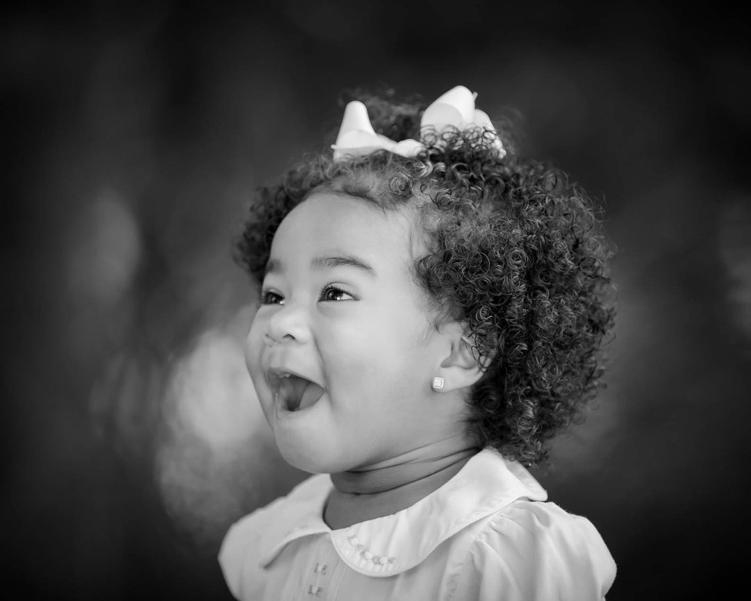 Candid portrait of a laughing child looking off to the side, captured in natural light with a warm, fine art style.