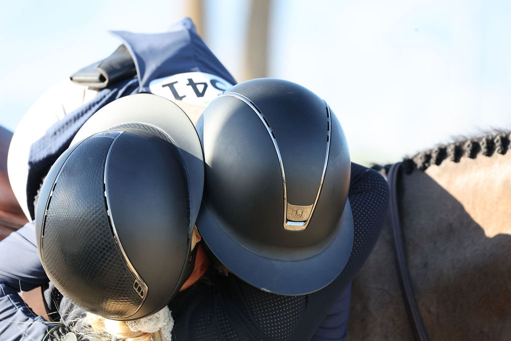 Black and white close-up of an equestrian rider and horse with helmets in the foreground.