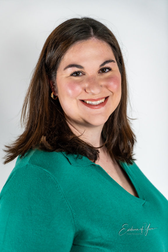 Smiling person with long brown hair wearing a green top against a white background.