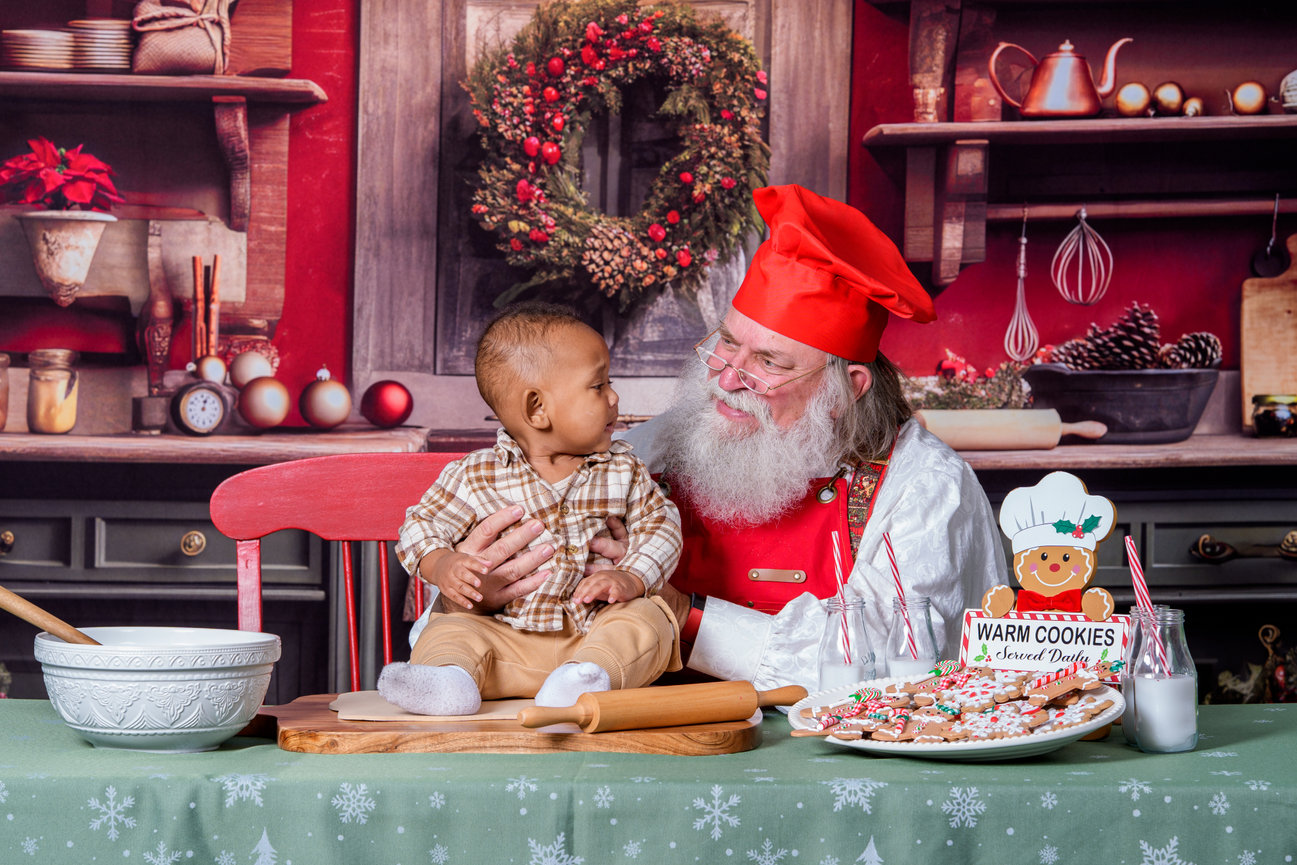 Holiday portrait of toddler with Santa Claus in festive kitchen setup, part of professional Santa mini sessions at photography studio