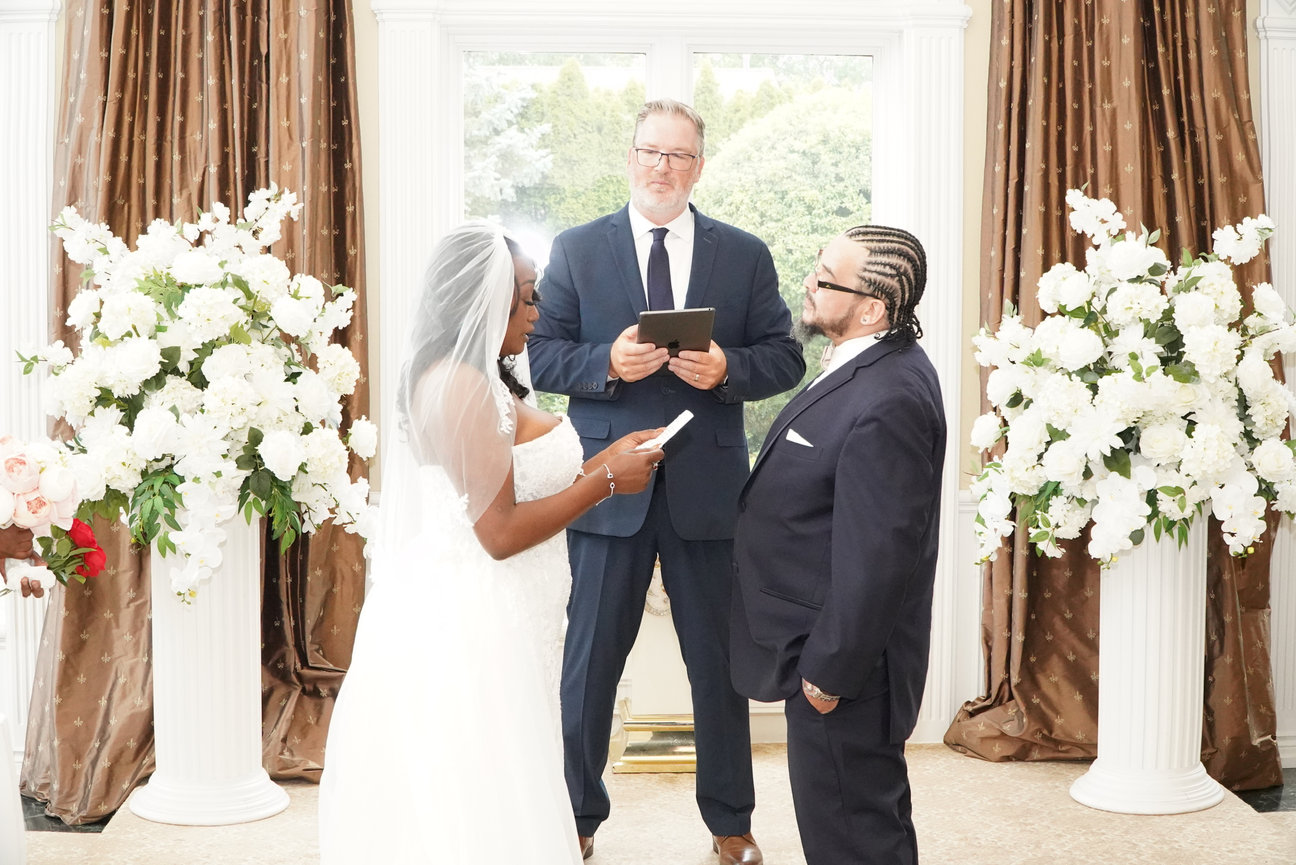 Wedding couple exchanging vows with officiant in a floral indoor ceremony setting