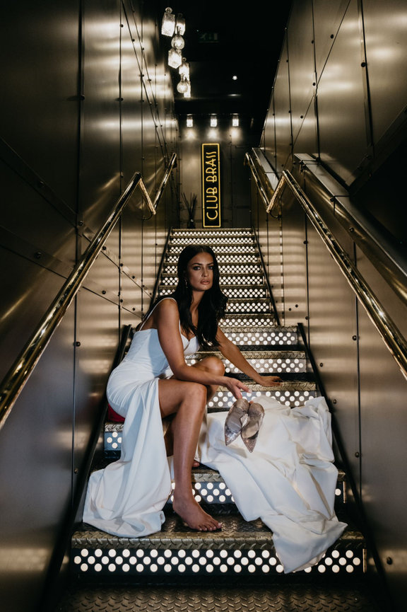 Editorial Manchester wedding photography at Club Brass featuring a bride on illuminated stairs with her heels in hand.