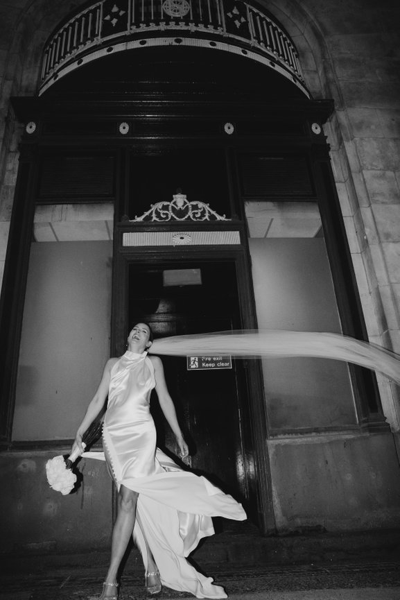 Timeless black and white bridal portrait; a joyful moment caught in motion with a flowing veil and editorial, unfiltered energy.