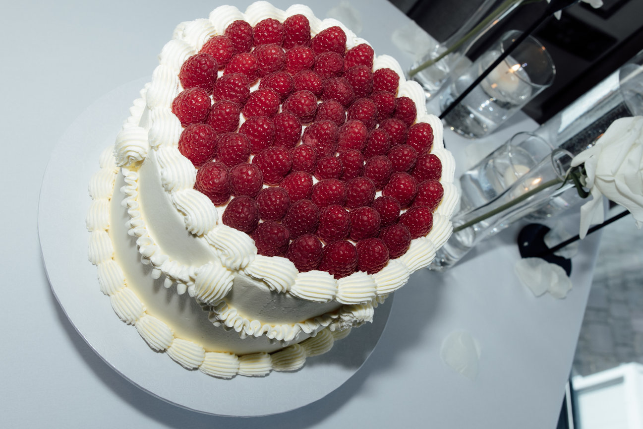 Close-up of a two-tiered white wedding cake topped with fresh raspberries on a decorated table at Hope Street hotel using modern flash photography.