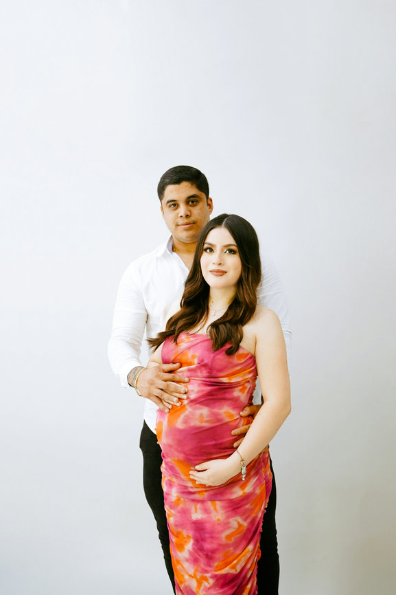 Pregnant couple posing together against a white background