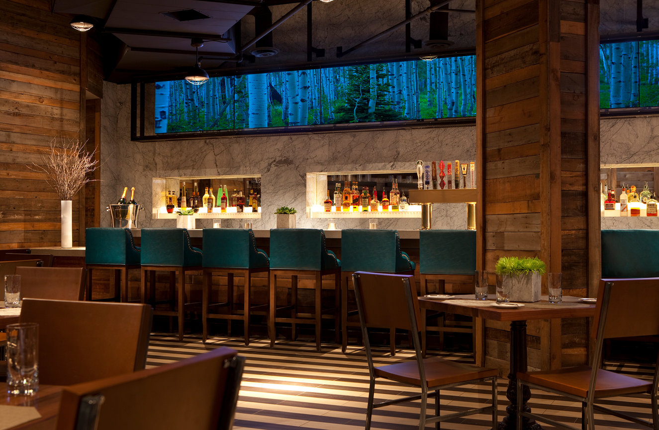 Restaurant in Minnesota with Wood Walls and Bar featuring a marble Wall with a long Screen above bar showcasing a mixture of landscape videos.