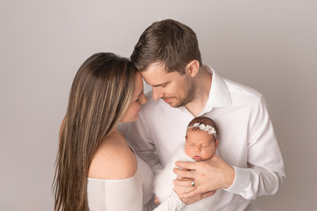 Studio family portrait with parents embracing newborn, capturing joy and tenderness in neutral-toned setting