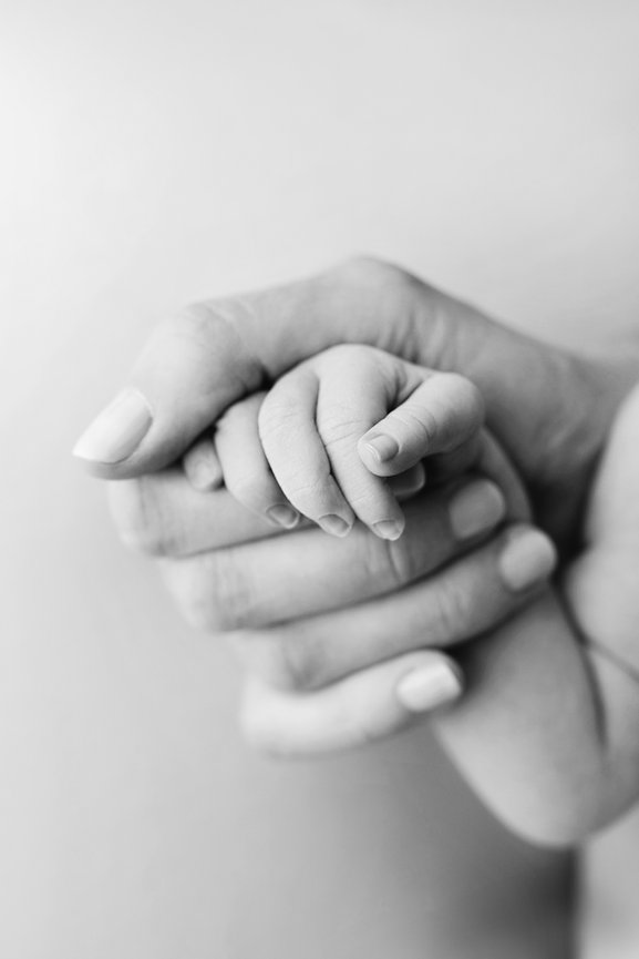 Tender moment between mom and newborn baby holding hands.