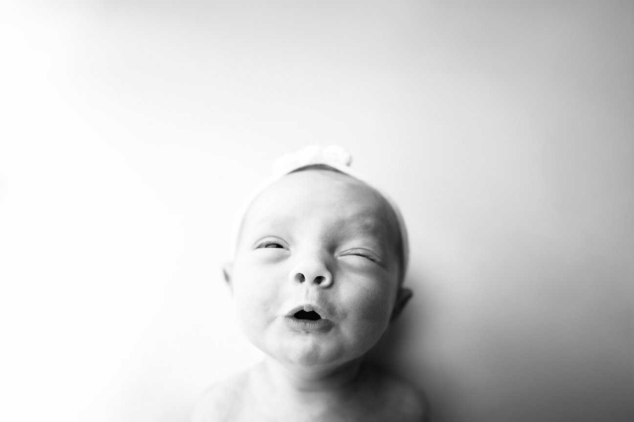 Black and white photo of newborn smirking at one week old, showcasing sweet and silly moments in studio